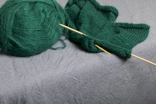 Knitting with wooden knitting. A ball of dark green thread and wooden knitting needles in an unfinished knit.