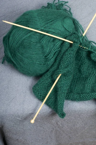 Knitting with wooden knitting. A ball of dark green thread and wooden knitting needles in an unfinished knit.