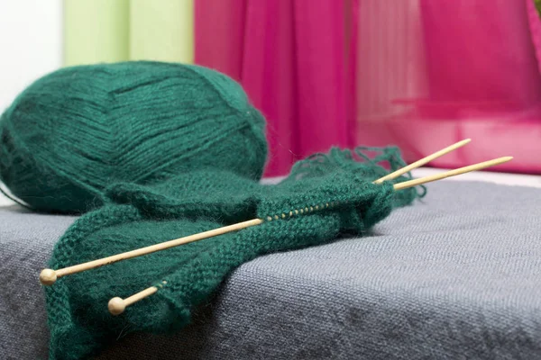 Knitting with wooden knitting. A ball of dark green thread and wooden knitting needles in an unfinished knit.