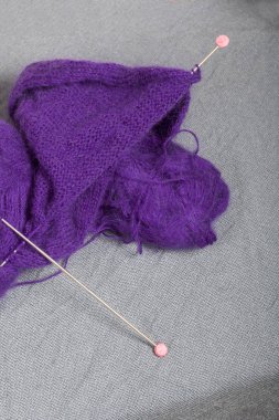 Çelik örgü iğneleri ile örgü. Bir top mor iplik ve bitmemiş bir örme çelik örgü iğneler.