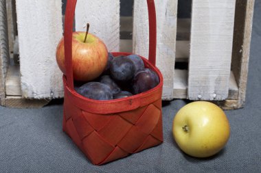 Olgun aromatik Erik ve elma bir hasır sepet içinde. Panoları dışarı knocked ahşap kutusunun yakınında bulunan.