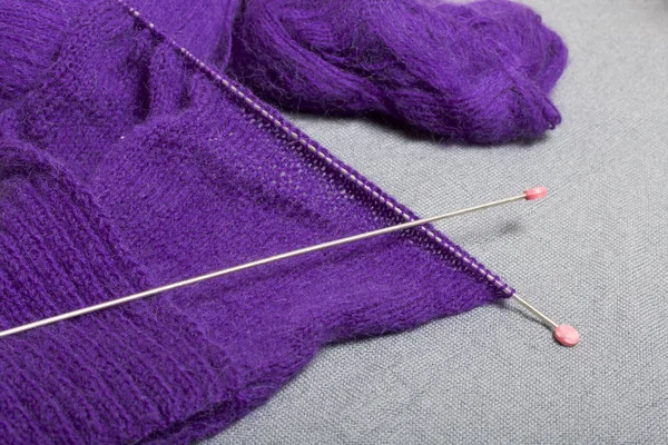 Knitting with steel knitting needles. A ball of purple thread and steel knitting needles in an unfinished knit.