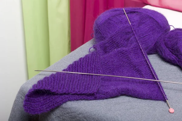 Knitting with steel knitting needles. A ball of purple thread and steel knitting needles in an unfinished knit.