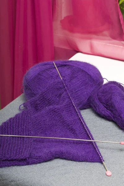 Knitting with steel knitting needles. A ball of purple thread and steel knitting needles in an unfinished knit.