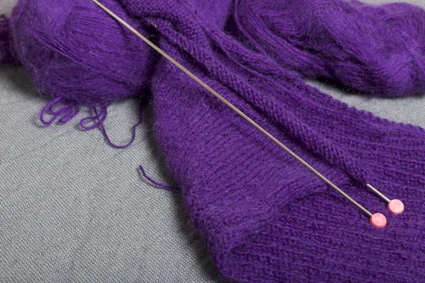 Knitting with steel knitting needles. A ball of purple thread and steel knitting needles in an unfinished knit.