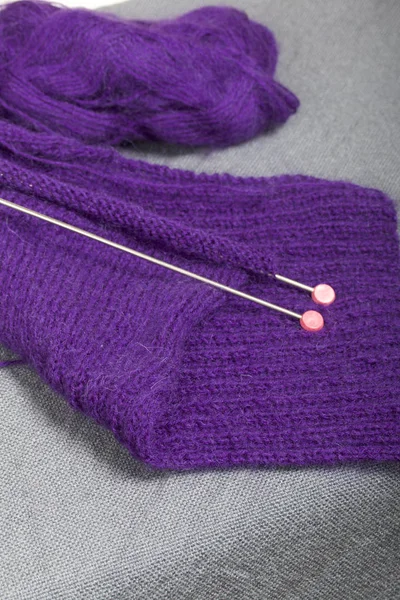 Knitting with steel knitting needles. A ball of purple thread and steel knitting needles in an unfinished knit.