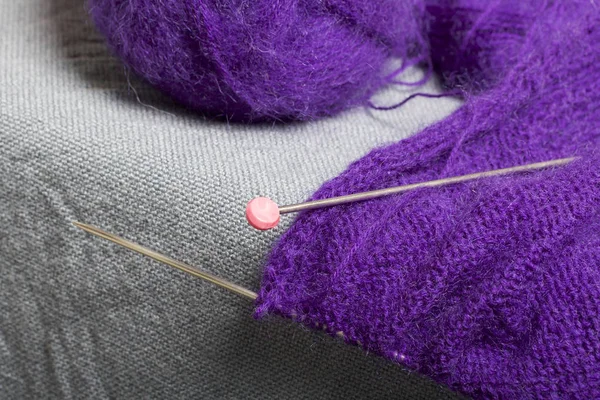 Knitting with steel knitting needles. A ball of purple thread and steel knitting needles in an unfinished knit.