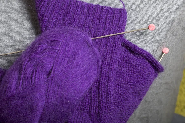 Knitting with steel knitting needles. A ball of purple thread and steel knitting needles in an unfinished knit.