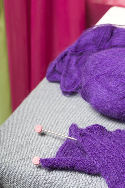 Knitting with steel knitting needles. A ball of purple thread and steel knitting needles in an unfinished knit.