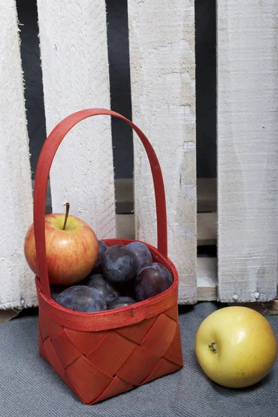 Ripe aromatic plums and apples in a wicker basket. Located near the wooden box knocked out of the boards.