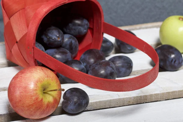 Ripe fragrant plums and apples crumbled out of a wicker basket. Located on a wooden box, knocked out of the boards.