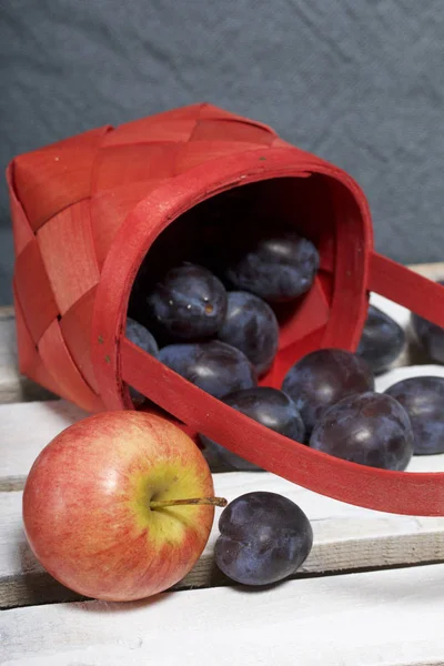 Ripe fragrant plums and apples crumbled out of a wicker basket. Located on a wooden box, knocked out of the boards.