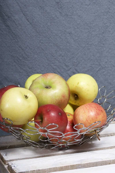 Ripe aromatic apples in a steel basket. Located on a wooden box, knocked out of the boards.