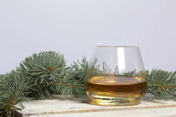 Blue spruce branches on a wooden box of boards, painted in white. Nearby is a glass of whiskey.