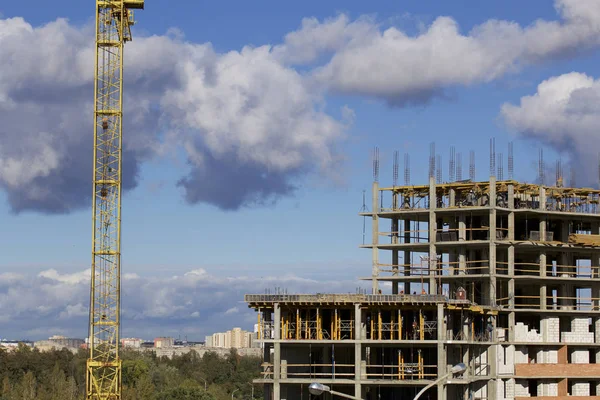 Tower cranes on the construction of a building with a frame of reinforced concrete. Sunlit against a blue sky.