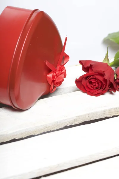 A bouquet of scarlet roses and a gift in a box in the shape of a heart. Flowers lie on a wooden box. On a white background.