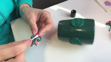  El sanatları polimer Clay. Bir kadın bir dekoratif polimer kil öğesi ile tutkal smear. Sonraki masaya polimer kil Dekoratif unsurları vardır. Polimer kil yapılan sıva ile dekore edilmiş kupa.