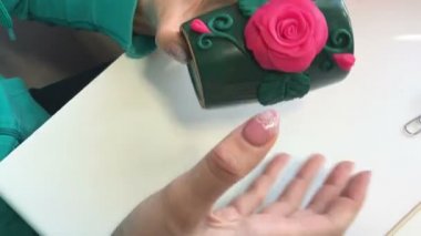 El sanatları polimer Clay. Bir kadın bir tutkal polimer kil çiçek Kupası için sopa ve bir tahta şiş ile düzeltiyor. Sonraki masaya polimer kil Dekoratif unsurları vardır. Polimer kil yapılan sıva ile dekore edilmiş kupa.