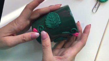 El sanatları polimer Clay. Bir kadın bir polimer kil dekoratif unsur Kupası için yapışır. Sonraki masaya polimer kil Dekoratif unsurları vardır. Polimer kil yapılan sıva ile dekore edilmiş kupa.