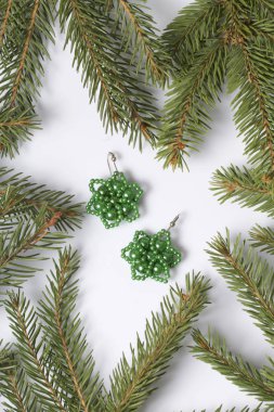 Kadın küpe boncuk Ladin dallar arasında yapılmış. Beyaz bir arka plan üzerinde.