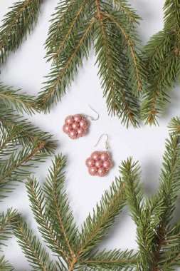 Kadın küpe boncuk Ladin dallar arasında yapılmış. Beyaz bir arka plan üzerinde.