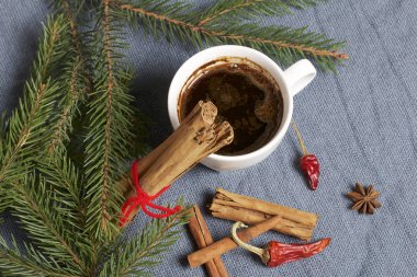 Bir fincan kahve masada. Tarçın ve bakla çam dalları yanındaki kırmızı biber. Dokuma bir arka plan üzerinde.