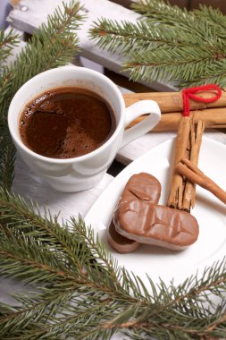 Bir fincan kahve, tarçın ve çam dalları yanında çikolata. Bir ahşap kutu.