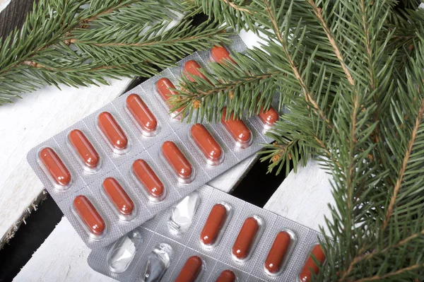 The blisters with pills. Different colors. Spruce  branches. On a wooden box.