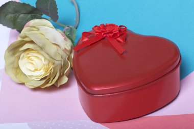 Bir hediye ile kırmızı bir kalp şeklinde bir kutu. Sonraki bir çiçektir. Çok renkli kağıt bir arka plan üzerinde.