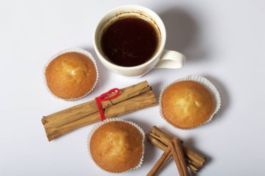 Bir bardak taze demlenmiş kahve ve çörek. Yakınlarda tarçın bulunmaktadır. Beyaz bir arka plan üzerinde.