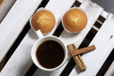 Bir bardak taze demlenmiş kahve ve çörek. Yakınlarda tarçın bulunmaktadır. Bir ahşap kutu üzerinde yer alan.