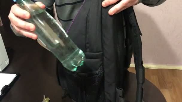 若い男は 彼のバックパックのポケットに水のボトルを置きます 彼はテーブル 携帯電話のキーをピックアップし — ストック動画