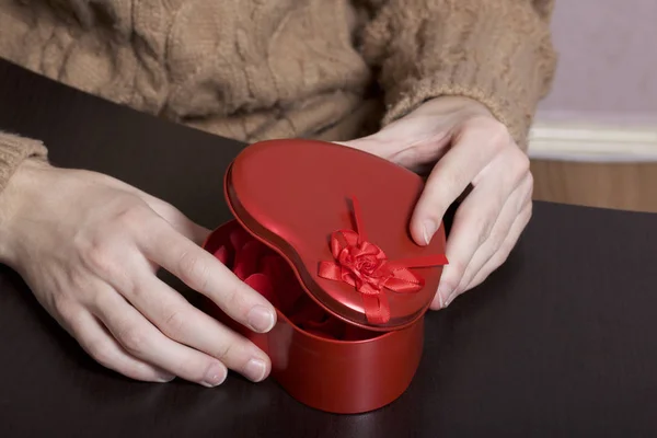 A young man opens a box with a gift. Box of tin, red. Made in the shape of a heart.