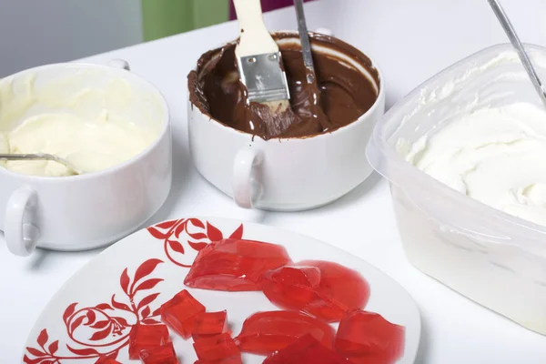 Melted white and black chocolate in white cups. Blender-ground curd and strawberry jelly on a plate. Stand for making dessert.