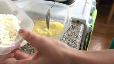 Bir kadın bir kapsayıcı eritilmiş tereyağı, vanilya ve pudra şekeri ile süzme peynir ekler. Tatlı için malzemeler.