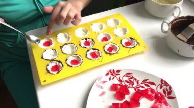 Bir kadın bir lor silikon kalıp çilekli jöle koyar. Kalıp eritilmiş beyaz ve koyu çikolata ile sürülür. Yakındaki çilekli jöle tabağa.
