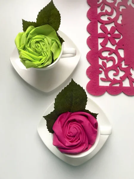Floral decorations using napkins. The finished flower is placed in a cup and decorated with green leaves.