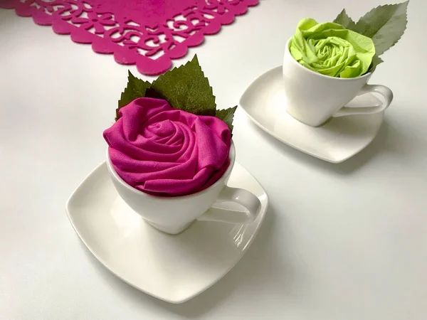 Floral decorations using napkins. The finished flower is placed in a cup and decorated with green leaves.