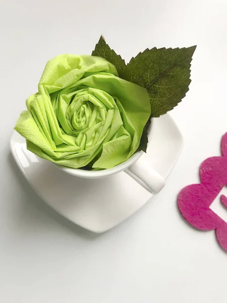 Floral decorations using napkins. The finished flower is placed in a cup and decorated with green leaves.