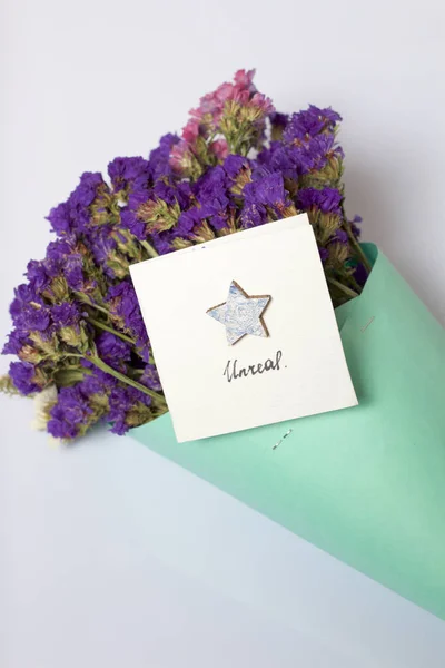 A bouquet of dried flowers, wrapped in colored paper. Near a small greeting card. On a white background.