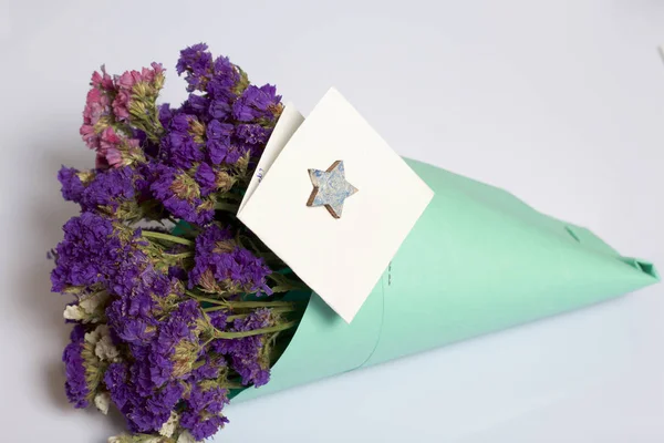 A bouquet of dried flowers, wrapped in colored paper. Near a small greeting card. On a white background.