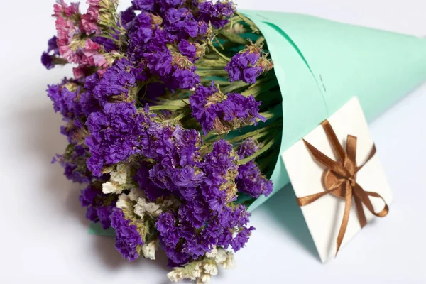 A bouquet of dried flowers, wrapped in colored paper. Near a small greeting card. On a white background.