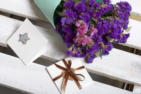 A bouquet of dried flowers, wrapped in colored paper. Near a small greeting card.