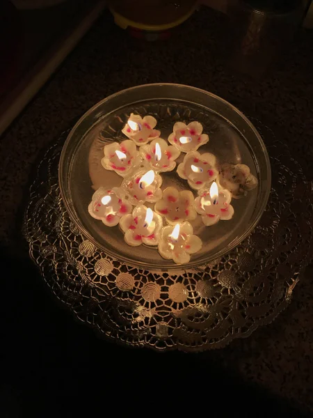 Burning candles in the shape of a flower are floating in the water.