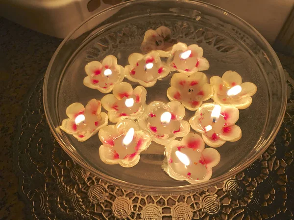 Burning candles in the shape of a flower are floating in the water.