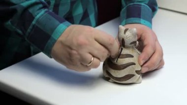 Bir kedi şeklinde bir kumbara geçerli. Bir adam paralar elinde tutuyor ve onları bir kumbara koyar.