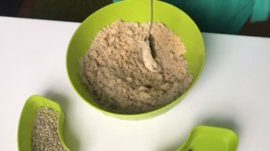 Bir kadın bal kaşığı ezilmiş fıstık ve Ayçiçeği çekirdeği ile bir kap içinde ekler. Helva yapmak için karışımları.