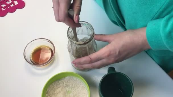 女性は ガラス瓶の中の液体の蜂蜜と小麦粉を混ぜています 家庭でパンを焼く酵母の準備 その他の食材がテーブルの近く — ストック動画