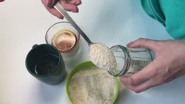 女性は ガラスの瓶に小麦粉の杯を置きます 家庭でパンを焼く酵母の準備 その他の食材がテーブルの近く — ストック動画
