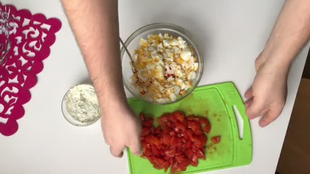 A man adds slices of tomatoes in a container with ingredients for salad. Cooking salad of crab sticks, cheese, eggs and tomatoes. — Stock Footage Man Adds Slices Tomatoes Container Ingredients Salad Cooking Salad Crab Royalty Free Stock Footage